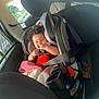 Truth is registered to the contest to win money with this photo: baby, car_seat, child, curly_hair, red_clothing, blanket, seatbelt, car_interior, smiling, happy, black_bow, infant, playful, sunlight, window, seat, travel, cute, portrait, child_safety