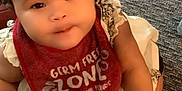 Truth joined the competition — help win amazing prizes! baby, child, infant, headband, bib, white_dress, carpet, sitting, cute, smiling, hand, curly_hair, indoor, young_child, person, face, looking_up, red_bib, skin, clothing