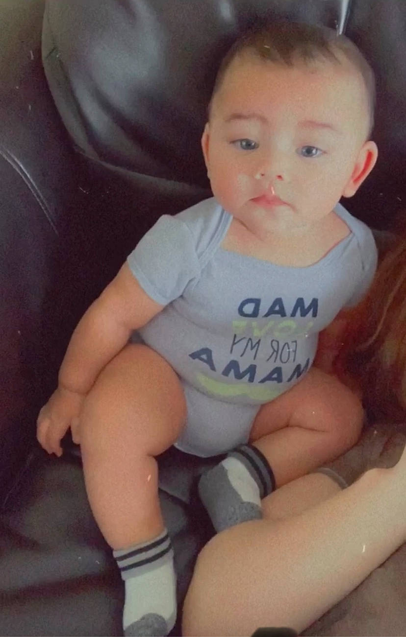 Keon is registered to the contest to win money with this photo: arm, baby, baby_toddler_clothing, brown_hair, cheek, child, comfort, ear, finger, hand, human_body, joint, knee, lap, mammal, person, sitting, skin, sock, thigh