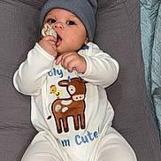 Ace is registered to the contest to win money with this photo: baby, beanie, child, cute, deer, gray, headwear, infant, lying_down, onesie, pacifier, person, plush, resting, soft, teether, white_clothing, young_child, indoor, comfort