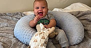 Ace joined the competition — help win amazing prizes! baby, smiling, plush_toy, blanket, cushion, gray, blue, clothing, sitting, indoor, happy, child, infant, person, footwear, pacifier, neutral_background, cute, portrait, cozy