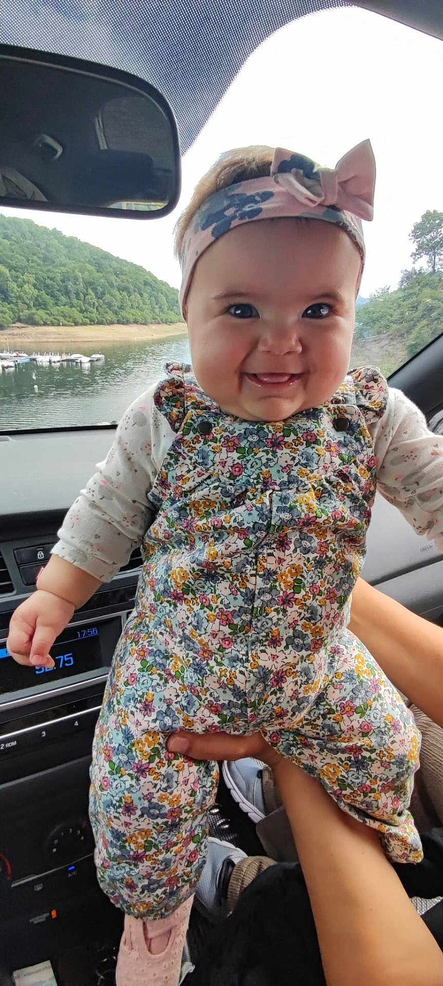 Melina Gisel a rejoint le concours — aidez-le/la à gagner de superbes lots ! baby, child, smiling, headband, bow, floral_outfit, car_interior, hand_holding, lake_view, green_hills, window, seat, footwear, cute, portrait, happy, person, indoors, nature, scenic_view