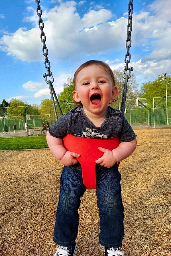 Braxton is registered to the contest to win money with this photo: blue, cloud, eye, face, facial_expression, finger, grass, hair, happy, head, human_body, leisure, people_in_nature, person, plant, skin, sky, smile, swing, toddler