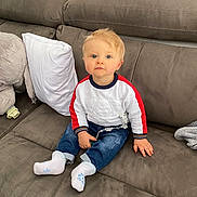 Logan a rejoint le concours — aidez-le/la à gagner de superbes lots ! toddler, child, couch, indoor, blue_eyes, blonde_hair, sweater, jeans, socks, pillow, home, furniture, person, baby, seated, cute, looking_at_camera, casual_clothing, living_room, soft_lighting