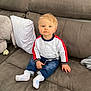 toddler, child, couch, indoor, blue_eyes, blonde_hair, sweater, jeans, socks, pillow, home, furniture, person, baby, seated, cute, looking_at_camera, casual_clothing, living_room, soft_lighting