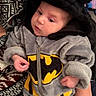 Lévanna a rejoint le concours — aidez-le/la à gagner de superbes lots ! baby, infant, batman_costume, hood, fuzzy_clothing, child, person, hands, patterned_sweater, couch, indoor, cute, costume, holding, small_hands, soft_texture, face, eyes, seated, cozy