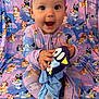 baby, child, onesie, headband, plush_toy, penguin, smile, happy, sitting, cartoon_pattern, background, purple, blue, pink, fabric, cute, infant, clothing, indoors, portrait