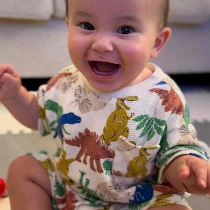 Jon Carlo joined the competition — help win amazing prizes! baby, background, child, clothing, couch, cute, dinosaur_print, expression, face, feet, hand, happy, head, indoors, infant, person, playmat, sitting, skin, smiling