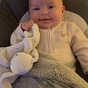 Mia participe au concours pour gagner de l'argent avec cette photo : baby, smiling, blanket, plush_toy, indoor, cute, child, soft_toy, warm_lighting, cozy, infant, face, clothing, comfort, happy, head, person, portrait, resting, cuddly