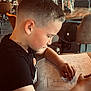 Naël participe au concours pour gagner de l'argent avec cette photo : child, boy, coloring, activity_sheet, table, cafe, people, hairstyle, short_hair, black_shirt, concentration, indoor, seated, hand, drawing, paper, background, furniture, casual, relaxed