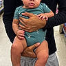 baby, child, person, holding, onesie, clothing, adult, hand, store, aisle, sweatpants, floor, indoor, casual, curious, serious, skin, portrait, human, shopping