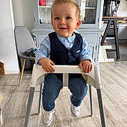 Adam a rejoint le concours — aidez-le/la à gagner de superbes lots ! toddler, child, high_chair, blue_shirt, vest, jeans, white_shoes, smile, indoor, kitchen, cabinet, glassware, wood_floor, chair, furniture, person, happy, portrait, casual, modern