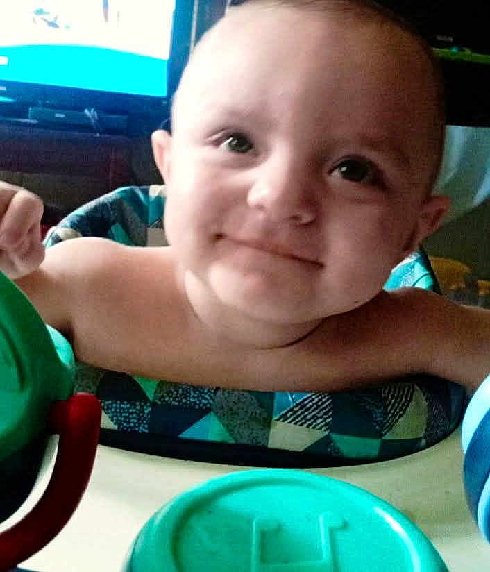 Ozzy is registered to the contest to win money with this photo: baby, child, smile, high_chair, toy, face, indoor, person, furniture, table, arm, head, expression, closeup, colorful, plastic, seat, happy, cute, young