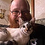 man, beard, glasses, cat, kitten, pet, smiling, indoor, lamp, mirror, wallpaper, couch, living_room, close_up, portrait, paws, furry, hand, happy, holding