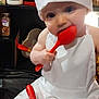 baby, chef_hat, apron, red_spoon, whisk, bowl, milk_bottle, kitchen, spice_jar, cooking, child, cute, chewing, white_clothing, indoor, person, smiling, blue_eyes, food_preparation, playful