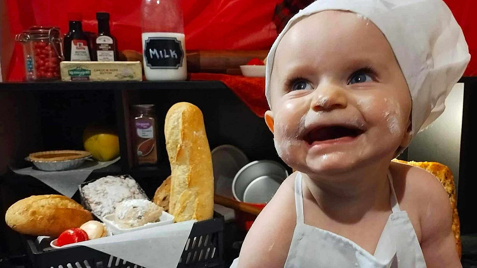 Nyx is registered to the contest to win money with this photo: baby, child, chef_hat, flour, smiling, bread, kitchen, apron, food, milk_jar, spices, happy, cooking, bakery, cute, person, indoor, grocery, table, ingredient