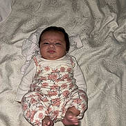 April is registered to the contest to win money with this photo: baby, infant, child, floral_clothing, blanket, patterned_blanket, lying_down, foot, cute, face, looking, curious, indoors, soft_lighting, newborn, person, sleepwear, small_feet, head, expression