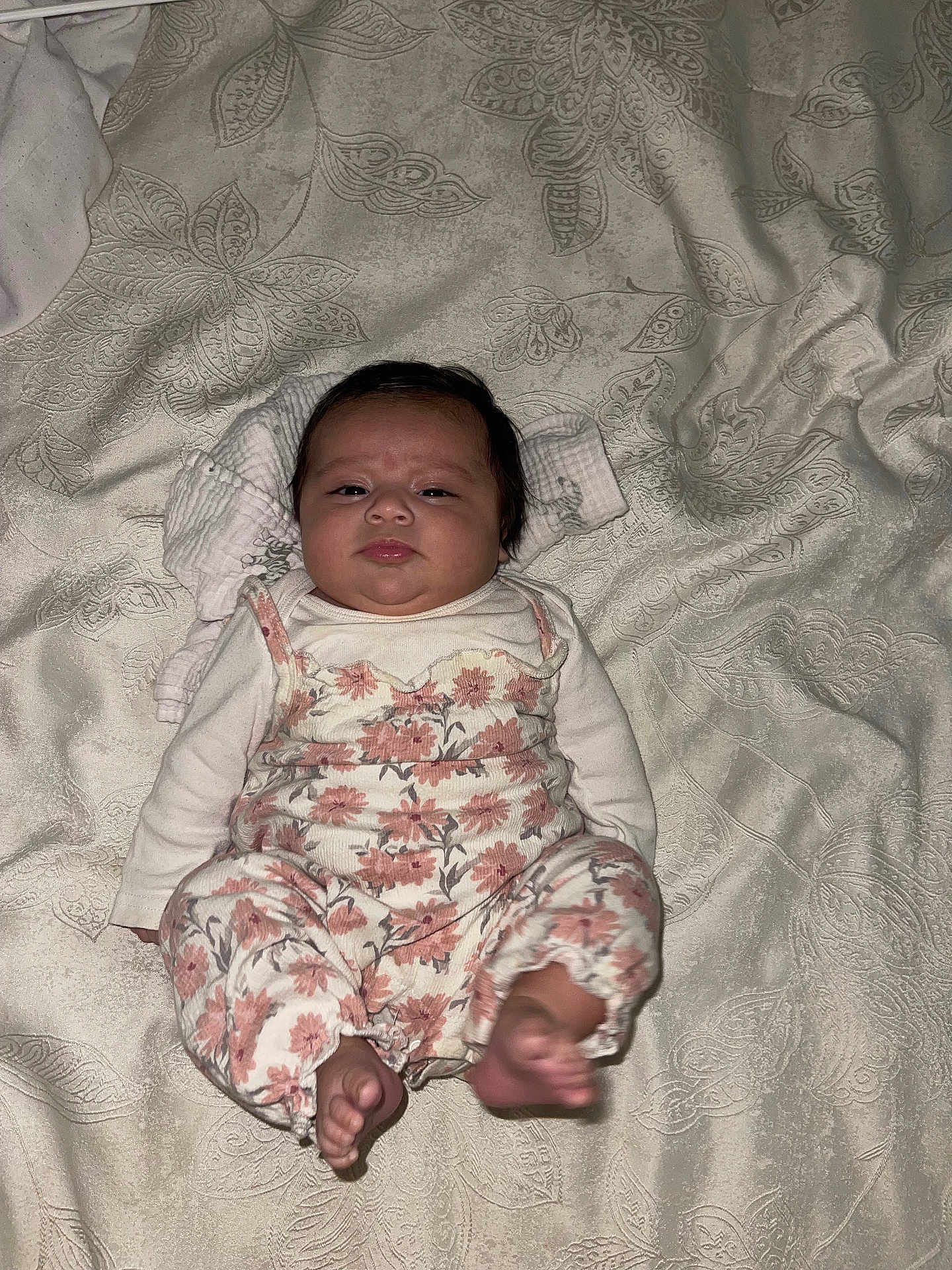 April is registered to the contest to win money with this photo: baby, infant, child, floral_clothing, blanket, patterned_blanket, lying_down, foot, cute, face, looking, curious, indoors, soft_lighting, newborn, person, sleepwear, small_feet, head, expression