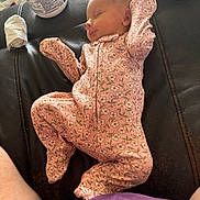 Chloe is registered to the contest to win money with this photo: baby, sleeping, onesie, pink_clothing, floral_pattern, leather_surface, baby_wipes, container, infant, peaceful, indoor, person, newborn, resting, fabric, closeup, cute, soft_lighting, skin, lying_down