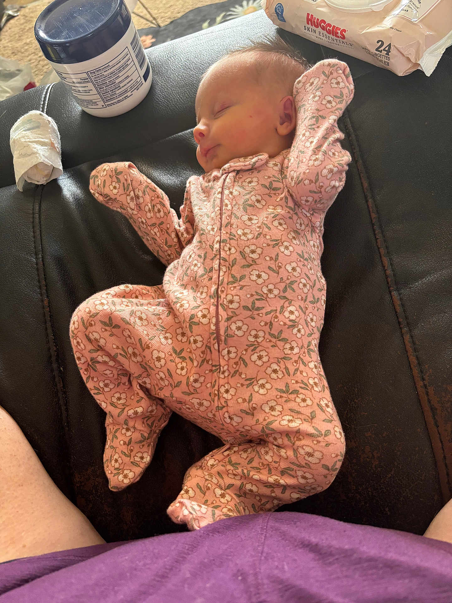 Chloe is registered to the contest to win money with this photo: baby, sleeping, onesie, pink_clothing, floral_pattern, leather_surface, baby_wipes, container, infant, peaceful, indoor, person, newborn, resting, fabric, closeup, cute, soft_lighting, skin, lying_down