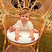Rosie a rejoint le concours — aidez-le/la à gagner de superbes lots ! baby, child, wicker_chair, lace_clothing, headband, outdoor, grass, cute, infant, sitting, portrait, smiling, furniture, natural_light, baby_face, expression, hands, feet, cushion, decorative_chair