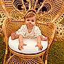 baby, child, wicker_chair, lace_clothing, headband, outdoor, grass, cute, infant, sitting, portrait, smiling, furniture, natural_light, baby_face, expression, hands, feet, cushion, decorative_chair