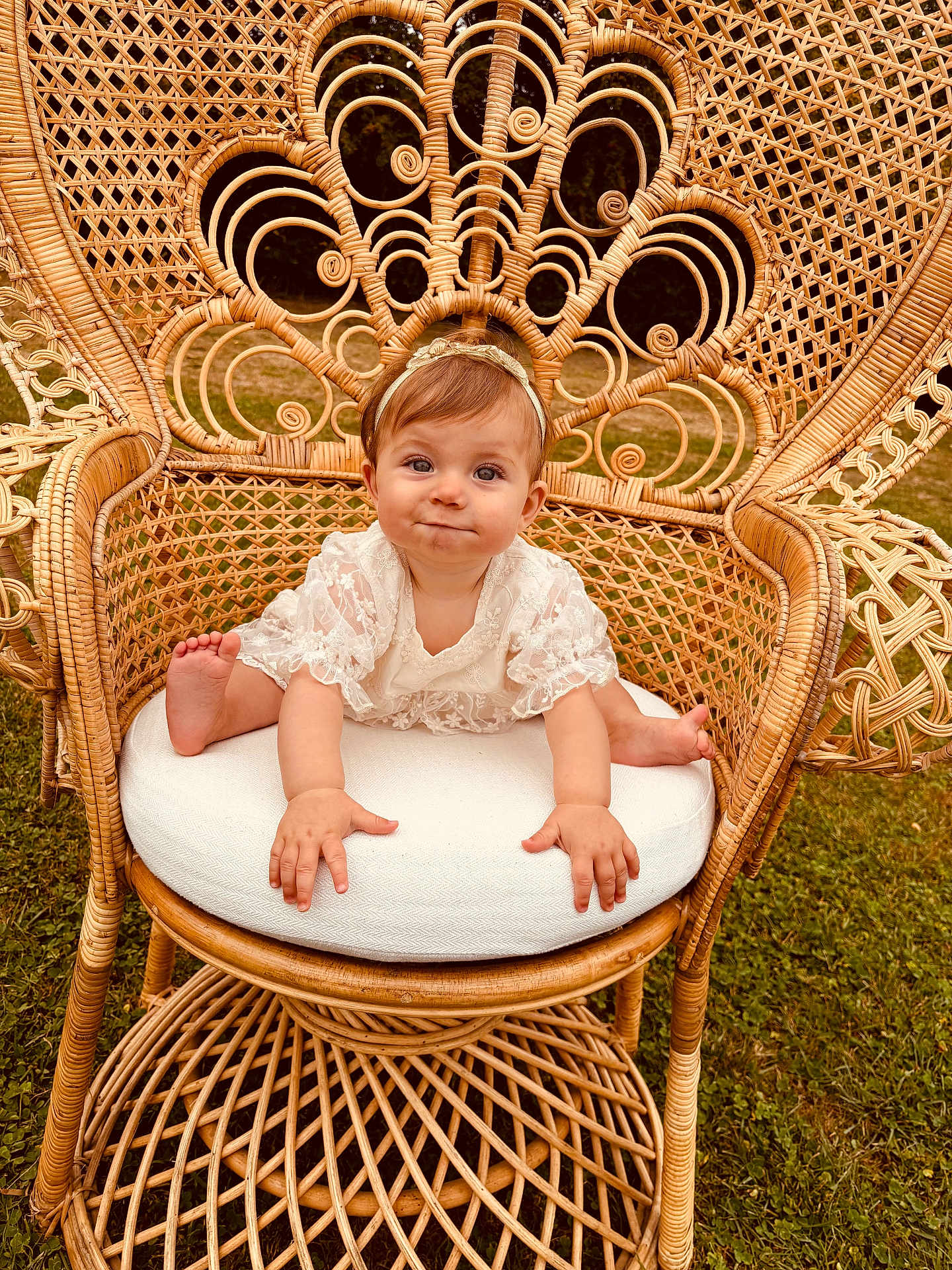 Rosie a rejoint le concours — aidez-le/la à gagner de superbes lots ! baby, child, wicker_chair, lace_clothing, headband, outdoor, grass, cute, infant, sitting, portrait, smiling, furniture, natural_light, baby_face, expression, hands, feet, cushion, decorative_chair