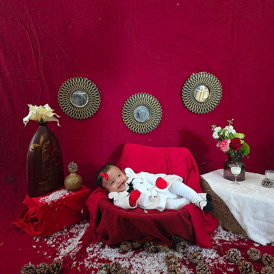 Alaia is registered to the contest to win money with this photo: baby, blanket, bow, couch, decorative_mirror, flowers, glass_jar, holiday_scene, indoor, infant, mittens, onesie, pinecones, portrait, props, red_backdrop, smiling, snow_flakes, table, vase