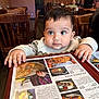 baby, child, menu, restaurant, table, wooden_chair, curious, hands, clothing, indoor, food_photos, menu_cover, person, cute, face, eyes, sweater, seated, dining, portrait