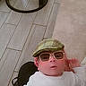 baby, baby_rocker, child, childwear, cute, digital_filter, expression, face, floor_tiles, fox_design, hand, headwear, indoors, infant, lying_down, person, plaid_cap, soft_surface, sunglasses_filter, white_outfit