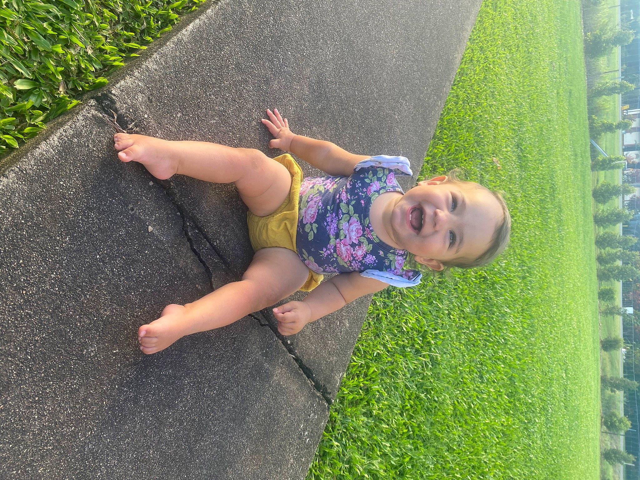 Skylar is registered to the contest to win money with this photo: arm, asphalt, barefoot, fun, grass, grass_family, green, hand, happy, human_body, lawn, leg, leisure, people_in_nature, person, plant, road_surface, shrub, sidewalk, toddler