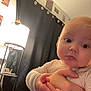 baby, child, indoor, lamp, curtain, hand, pajamas, person, face, light, cozy, expression, portrait, young_child, holding, wall, decor, sitting, candid, room