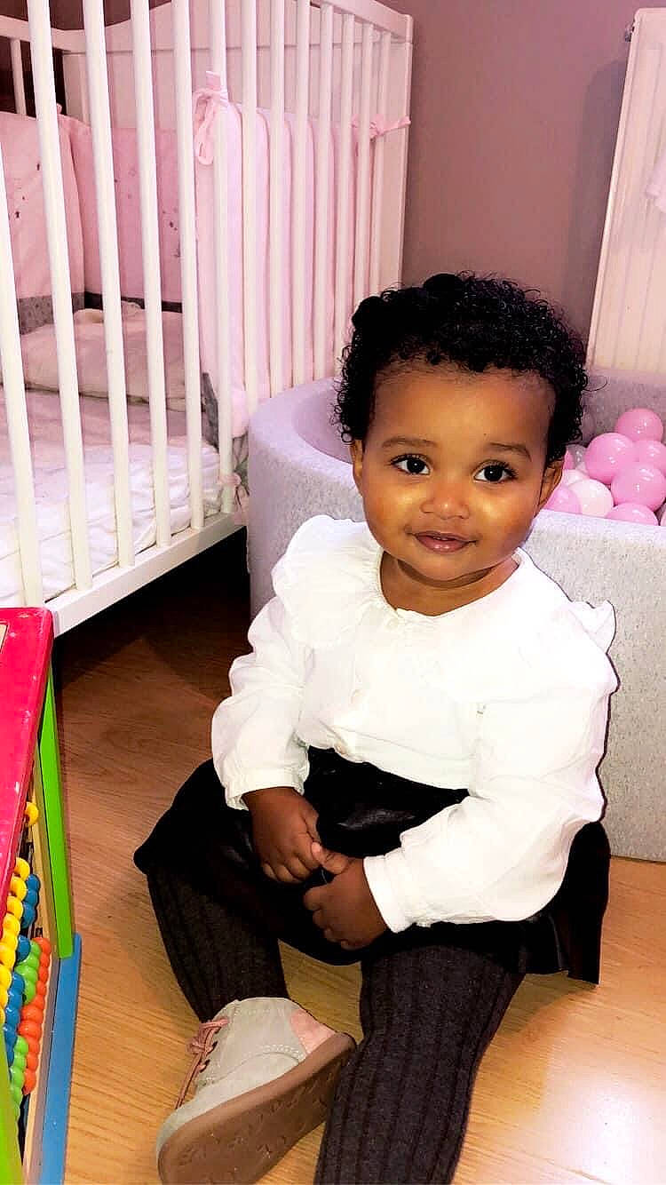 Lya a rejoint le concours — aidez-le/la à gagner de superbes lots ! baby, baby_toddler_clothing, black_hair, child, design, dress, eye, flooring, fun, happy, joy, knee, nursery, person, pink, room, sitting, skin, sleeve, smile