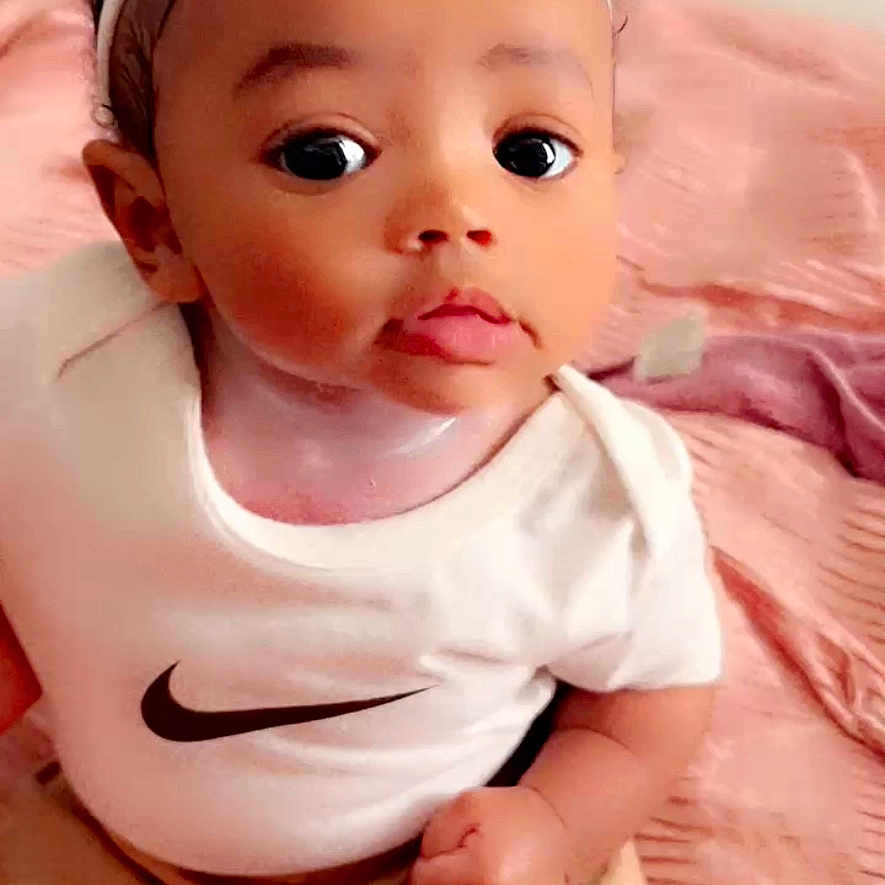 Zanylah joined the competition — help win amazing prizes! baby, blanket, child, clothing, curious_expression, cute, face, hand, headband, indoors, infant, nike_logo, person, pink_bow, portrait, sitting, skin, soft_texture, white_shirt, young_child
