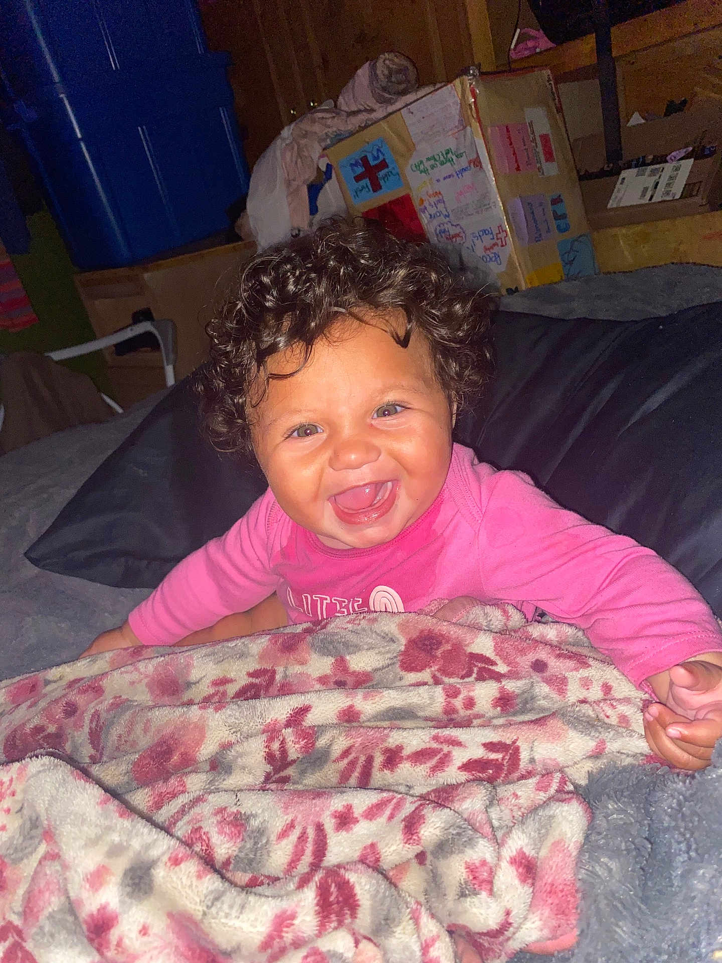 Ariyah is registered to the contest to win money with this photo: baby, curly_hair, smiling, blanket, bed, indoor, happy, child, person, pink_clothing, face, cheerful, portrait, infant, cozy, fabric, room, furniture, soft, wrapped
