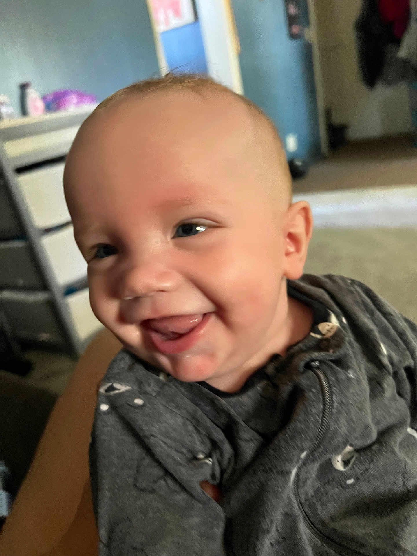 Aidyn joined the competition — help win amazing prizes! baby, smiling, indoor, child, face, tongue, clothing, grey_outfit, happy, person, infant, blurred_background, head, cute, young_child, closeup, expression, human, playful, portrait