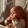 baby, child, high_chair, cookie, eating, food, hand, face, cushion, clothing, long_sleeves, indoor, natural_light, curious, chubby_cheeks, cute, portrait, infant, snack, soft_light