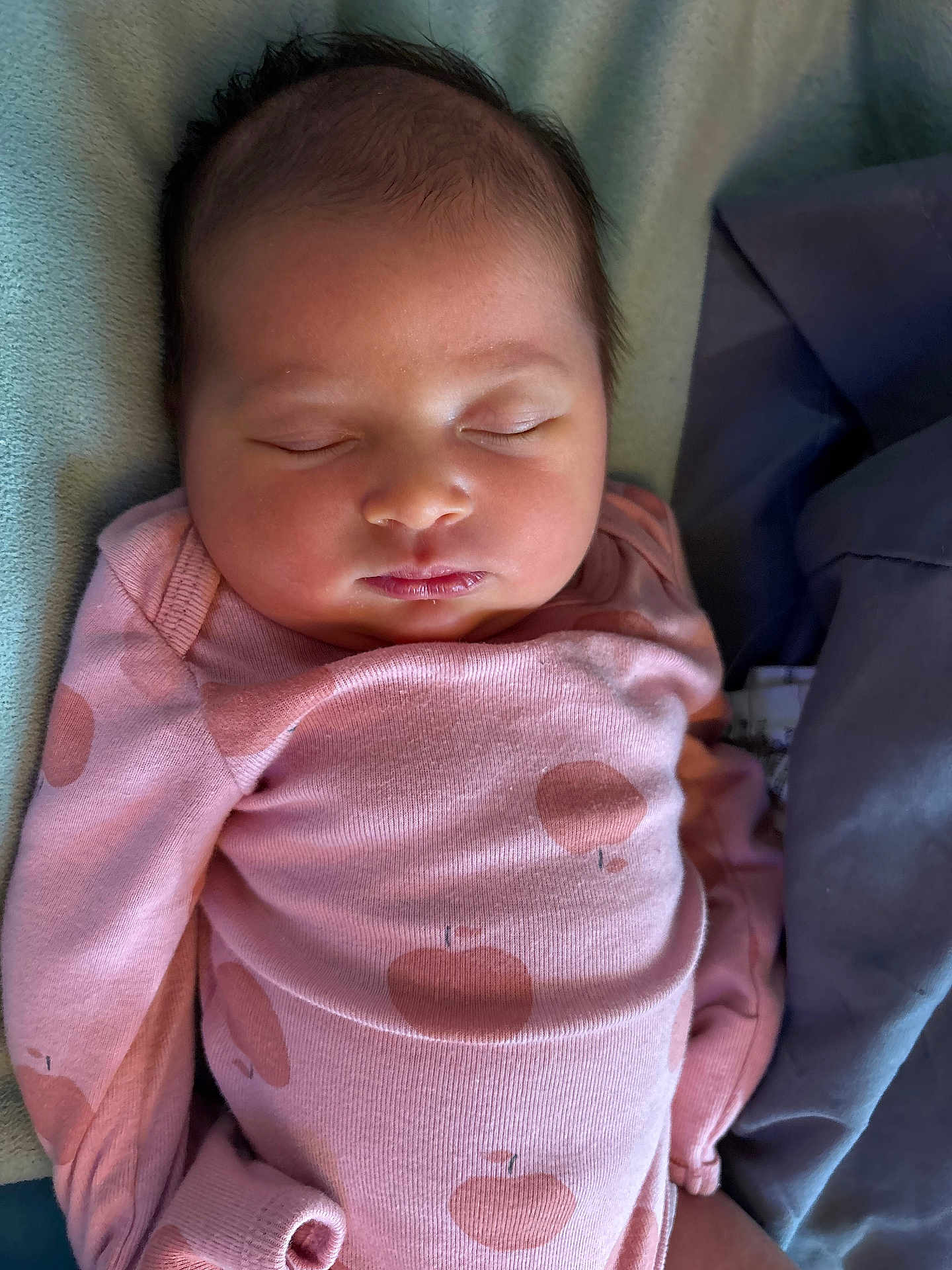 Nova is registered to the contest to win money with this photo: baby, sleeping, infant, pink_clothing, onesie, apple_pattern, close_up, face, peaceful, soft_texture, blanket, resting, newborn, cute, child, portrait, indoors, cozy, human, young