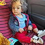 toddler, child, curly_hair, keys, car_seat, striped_cover, snack, smartphone, casual_clothing, denim_jacket, red_pants, white_shoes, indoor, seatbelt, window, car_door, toy, food, person, sitting