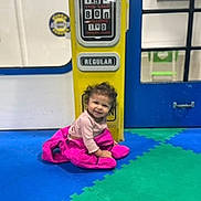 Bryelle joined the competition — help win amazing prizes! toddler, child, smiling, curly_hair, pink_jacket, yellow_gas_pump, regular_sign, foam_mats, blue_floor, green_floor, indoor, play_area, door, window, happy, person, floor, clothing, sitting, portrait