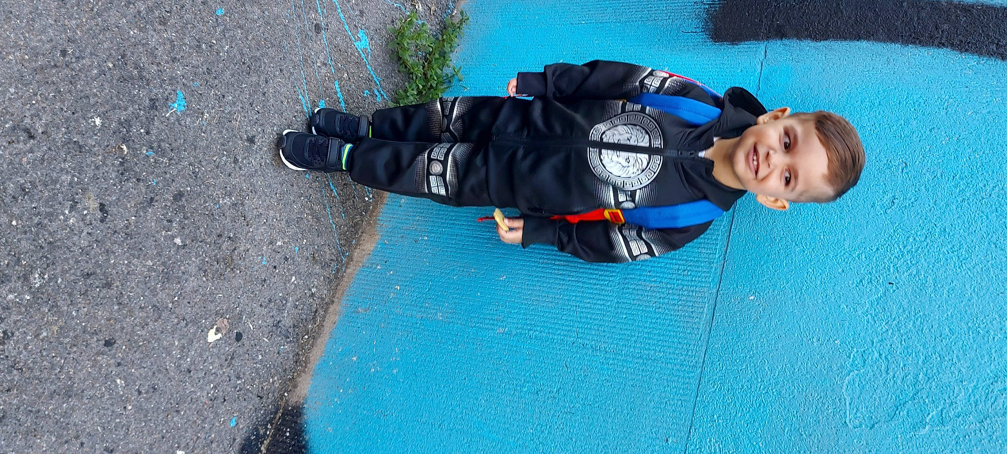 Timéo a rejoint le concours — aidez-le/la à gagner de superbes lots ! asphalt, azure, blue, concrete, electric_blue, flooring, fun, grass, jacket, joy, leisure, person, personal_protective_equipment, recreation, road_surface, shadow, sidewalk, smile, tar, toddler