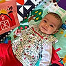 baby, child, playmat, toy, colorful, smiling, face, red_pants, patterned_clothing, indoor, farm_theme, barn, leafy_pattern, cute, infant, happy, lying_down, playful, hand, eyes