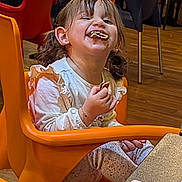 Maria a rejoint le concours — aidez-le/la à gagner de superbes lots ! child, girl, cookie, messy_face, orange_chair, pigtails, smiling, snack, indoor, table, wooden_floor, chairs, portrait, candid, long_sleeve_shirt, patterned_pants, earring, crumbs, happy, toddler