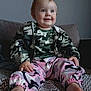 baby, blanket, camo_jacket, child, clothing, couch, cute, face, feet, happy, home, indoor, person, pink_pants, portrait, sitting, smile, toddler, young_child, zigzag_pattern