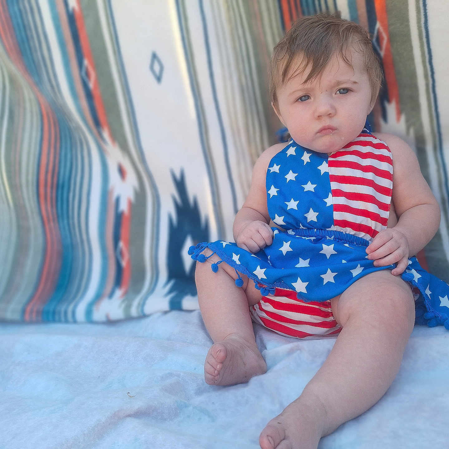 Dorothy is registered to the contest to win money with this photo: baby, blanket, child, clothing, cute, dress, fabric, face, foot, hand, indoors, infant, patriotic, patterned, portrait, serious, sitting, stars, stripes, young