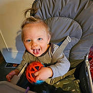 Jonas a rejoint le concours — aidez-le/la à gagner de superbes lots ! toddler, child, high_chair, toy, playful, indoor, happy, smiling, person, clothing, seat_belt, baby, furniture, face, hand, hair, blue_eyes, expression, table, plastic_toy