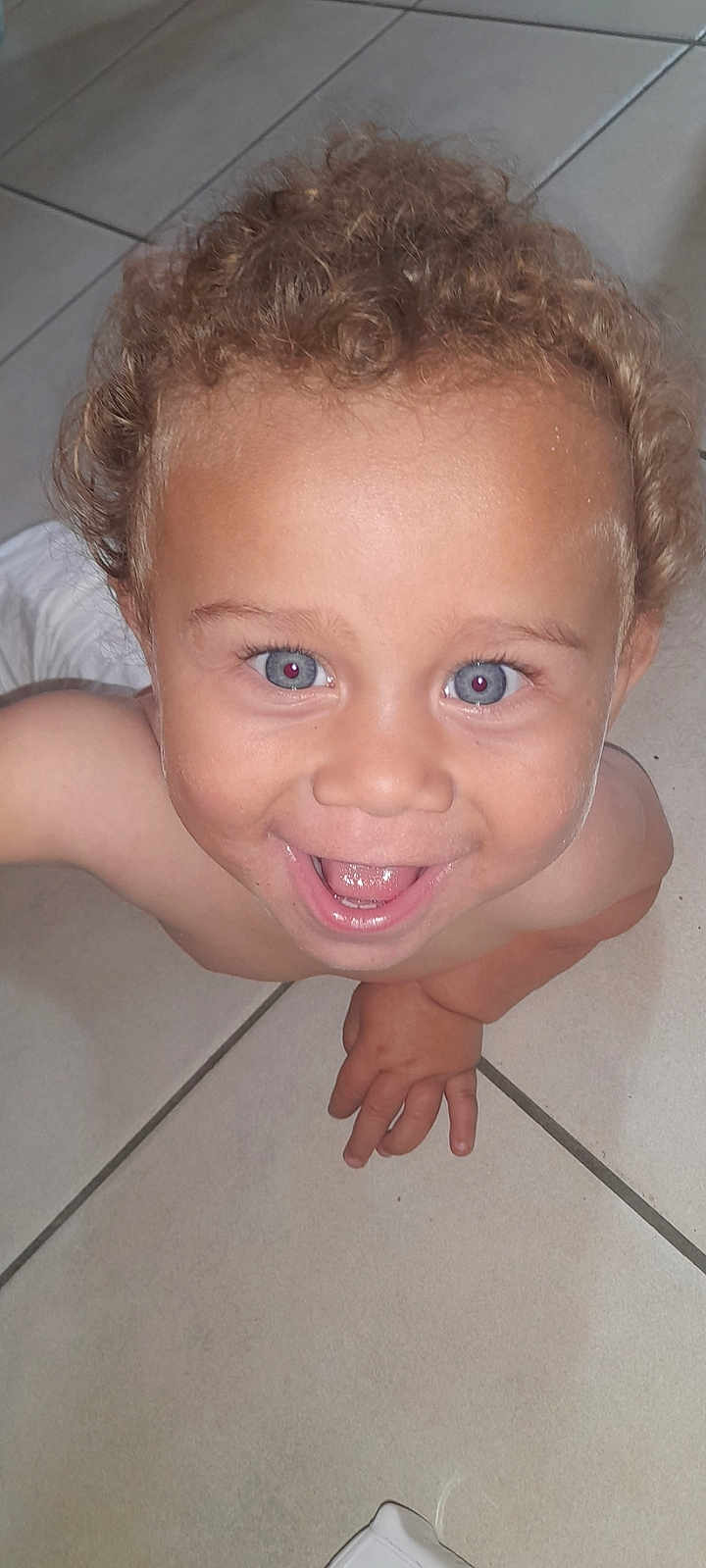 Saïan participe au concours pour gagner de l'argent avec cette photo : child, toddler, curly_hair, blue_eyes, smiling, happy, bare_chest, floor, tile_floor, hand, person, indoor, cute, young_child, skin, face, baby, playful, laughing, close_up