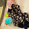Austin is registered to the contest to win money with this photo: baby, blue_toy, child, clothing, cozy, crib, cushion, cute, green_toy, happy, indoor, infant, lying_down, onesie, person, playful, plush_toy, skull_pattern, smile, soft_toy