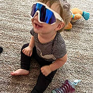 Drake joined the competition — help win amazing prizes! toddler, child, sunglasses, carpet, toy, stuffed_animal, sippy_cup, sitting, indoor, happy, smiling, clothing, striped_shirt, black_pants, barefoot, cute, playtime, home, fun, young_child