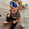 toddler, child, sunglasses, carpet, toy, stuffed_animal, sippy_cup, sitting, indoor, happy, smiling, clothing, striped_shirt, black_pants, barefoot, cute, playtime, home, fun, young_child